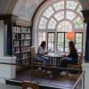 Image of Newnham students at a table in the Newnham Library. One reads while the other is on a laptop. 