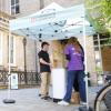 Two student workers and one visitor at the Open Day standing near the entrance to a University of Cambridge building, under a University of Cambridge branded gazebo