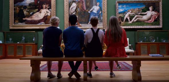 Students in museum sitting on bench observing paintings