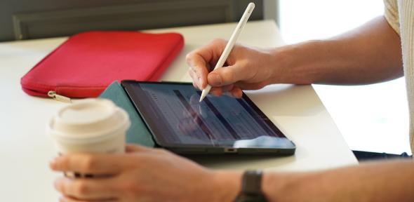 Coffee in one hand, stylus pen in other hand writing on computer screen