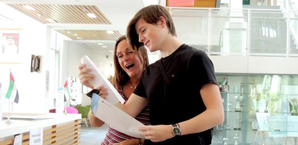 Student holding envelope and his exam results whilst his guardian expresses joy